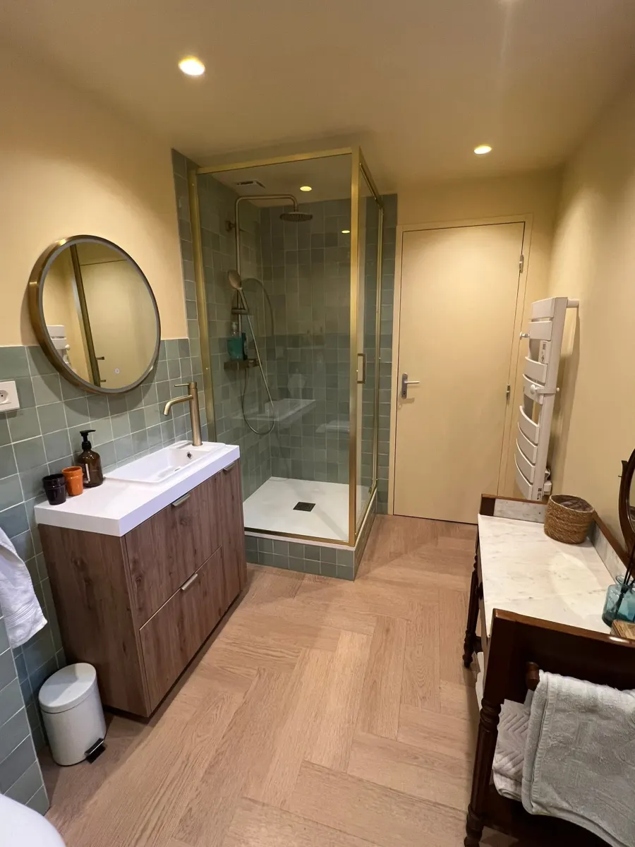 Vue d’ensemble de la salle de bains vert sauge avec douche vitrée et meuble vasque